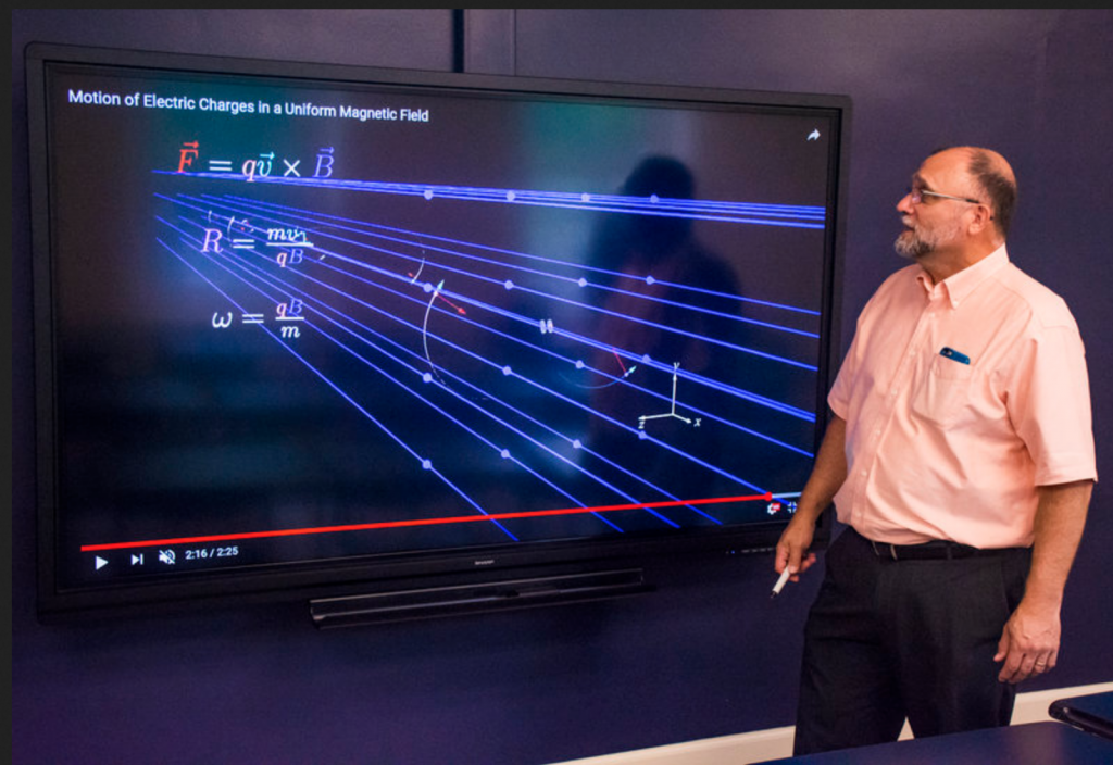 Screen showing a physics problem with Dr. Michael Gallis standing in front of it.